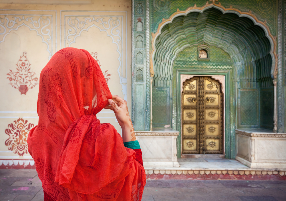 Mujer con un pañuelo rojo mirando una de la puertas del Palacio en Jaipur